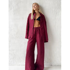 Burgundy long sleeve fabric shirt and matching drawstring trousers worn over a black top against a white textured wall.