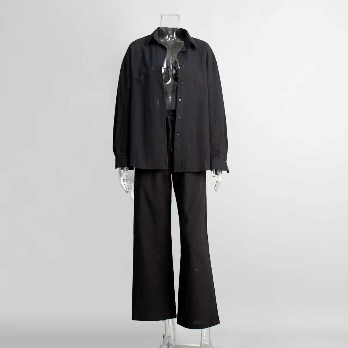 Black cotton two-piece suit with a long-sleeve button-down shirt and drawstring trousers on a clear mannequin.