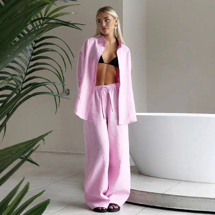 Woman wears a pink long sleeve lapel shirt and matching drawstring trousers over a black bikini top.