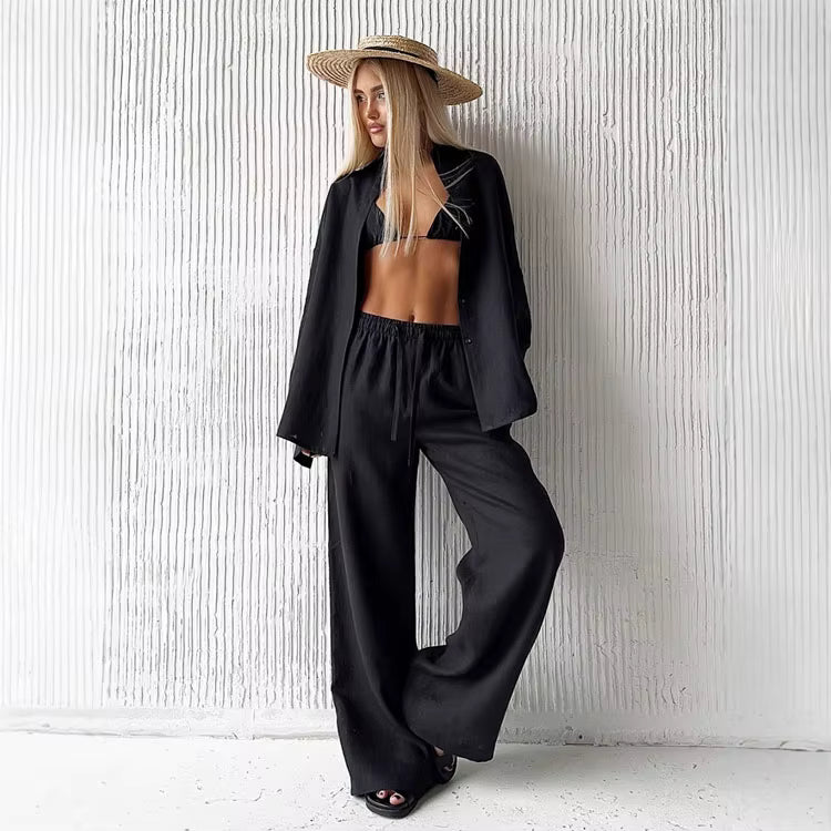 Woman wearing a black long sleeve fabric shirt and matching wide leg drawstring trousers with a straw hat.