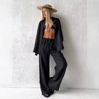 Woman wearing a black long sleeve fabric shirt and matching wide leg drawstring trousers with a straw hat.