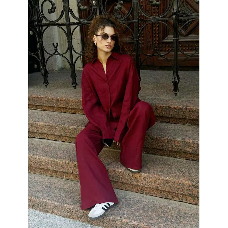 Woman sitting on stone steps wearing a dark red long sleeve lapel shirt and matching wide-leg trousers with white sneakers.